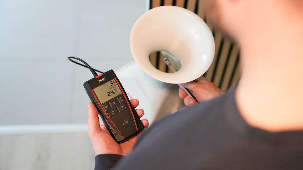 Medarbejder fra Jysk Ventilationsservice holder en tragt og et måleapparat som viser hvor godt ventilationsanlægget virker